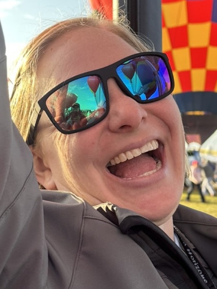 Amie laughing on the launch field, a balloon reflected in her sunglasses